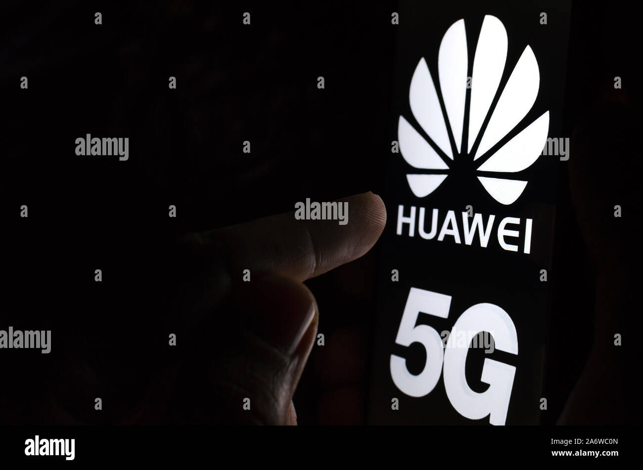 Huawei 5G logo on a smartphone screen in a dark room and a finger touching it. Stock Photo