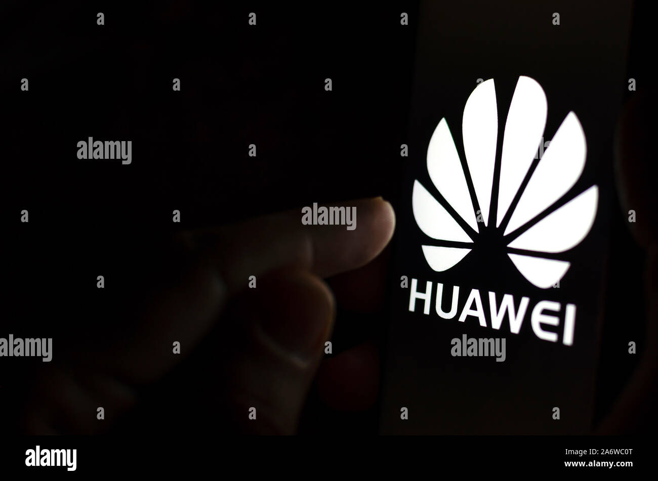 Huawei Logo on a smartphone screen in a dark room and a finger touching it. Stock Photo