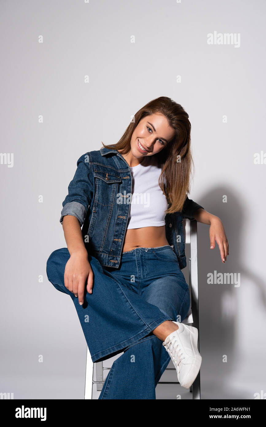 cheerful girl in denim jeans sitting on chair on white Stock Photo - Alamy
