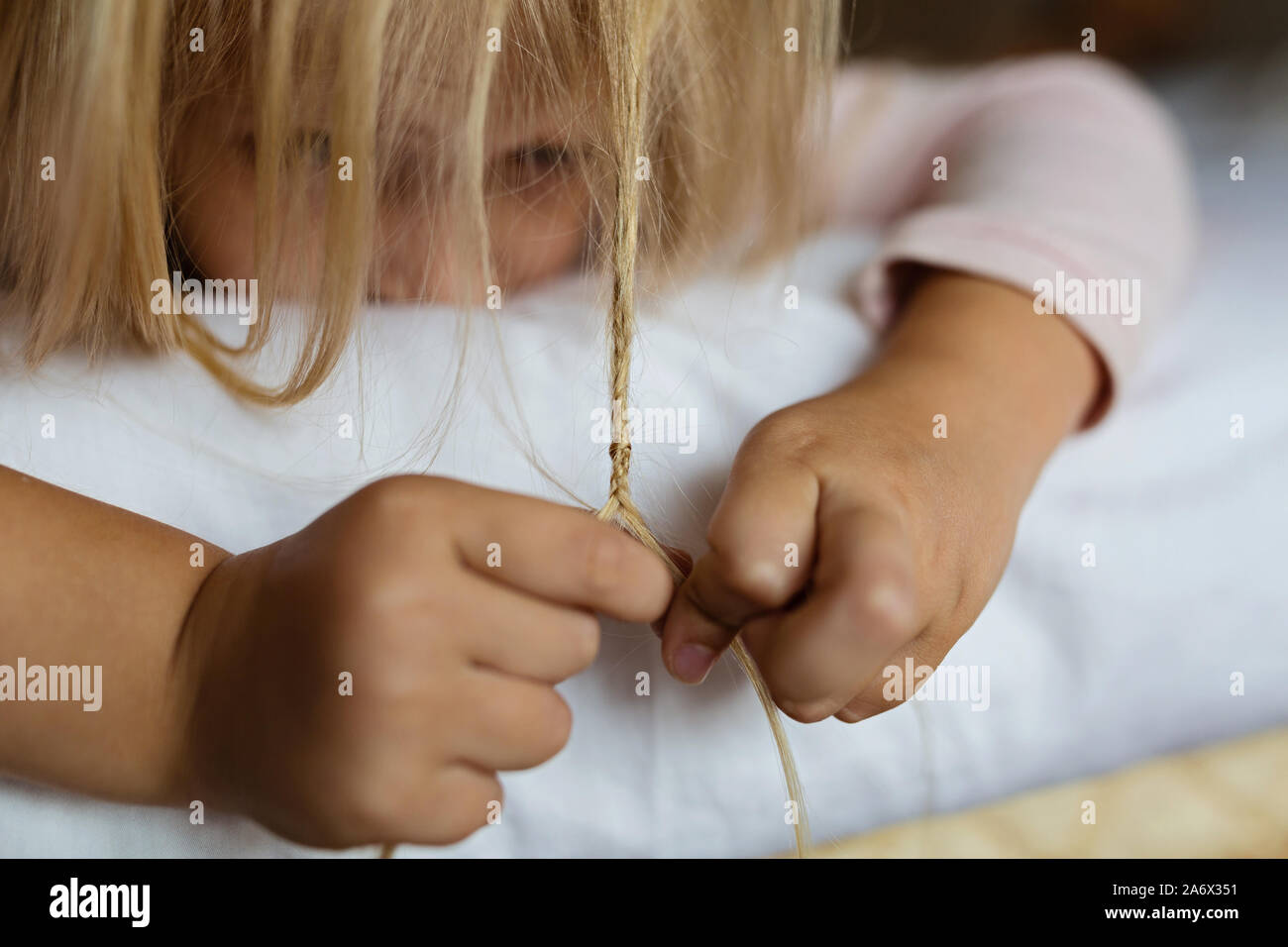 Cute blonde little girl in pajamas playing in white bed, early morning before going to kindergarten. Bedtime, playtime, relaxation concept Stock Photo