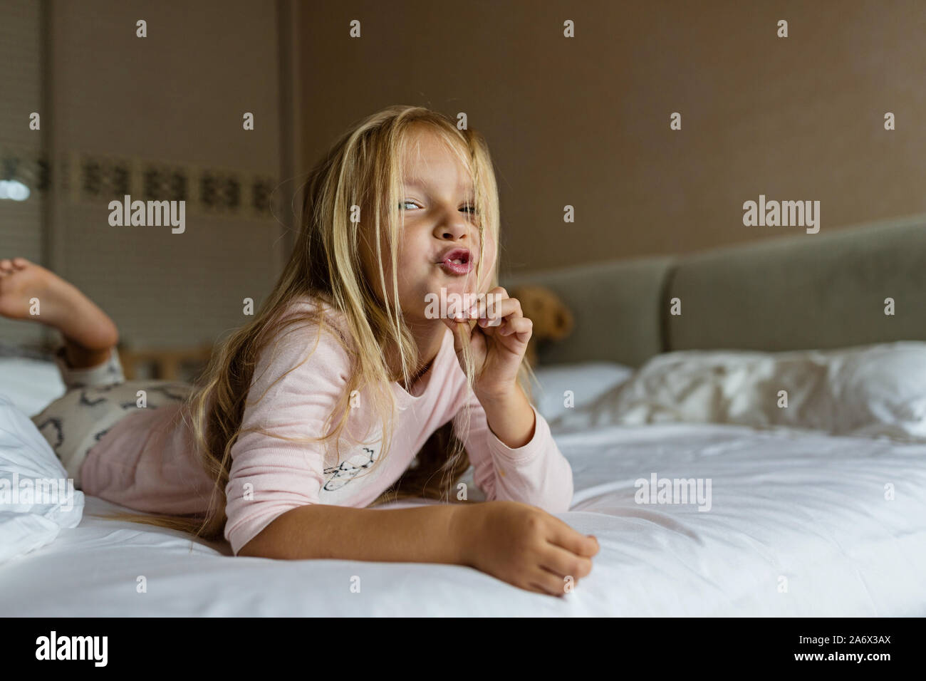 Cute blonde little girl in pajamas playing in white bed, early morning