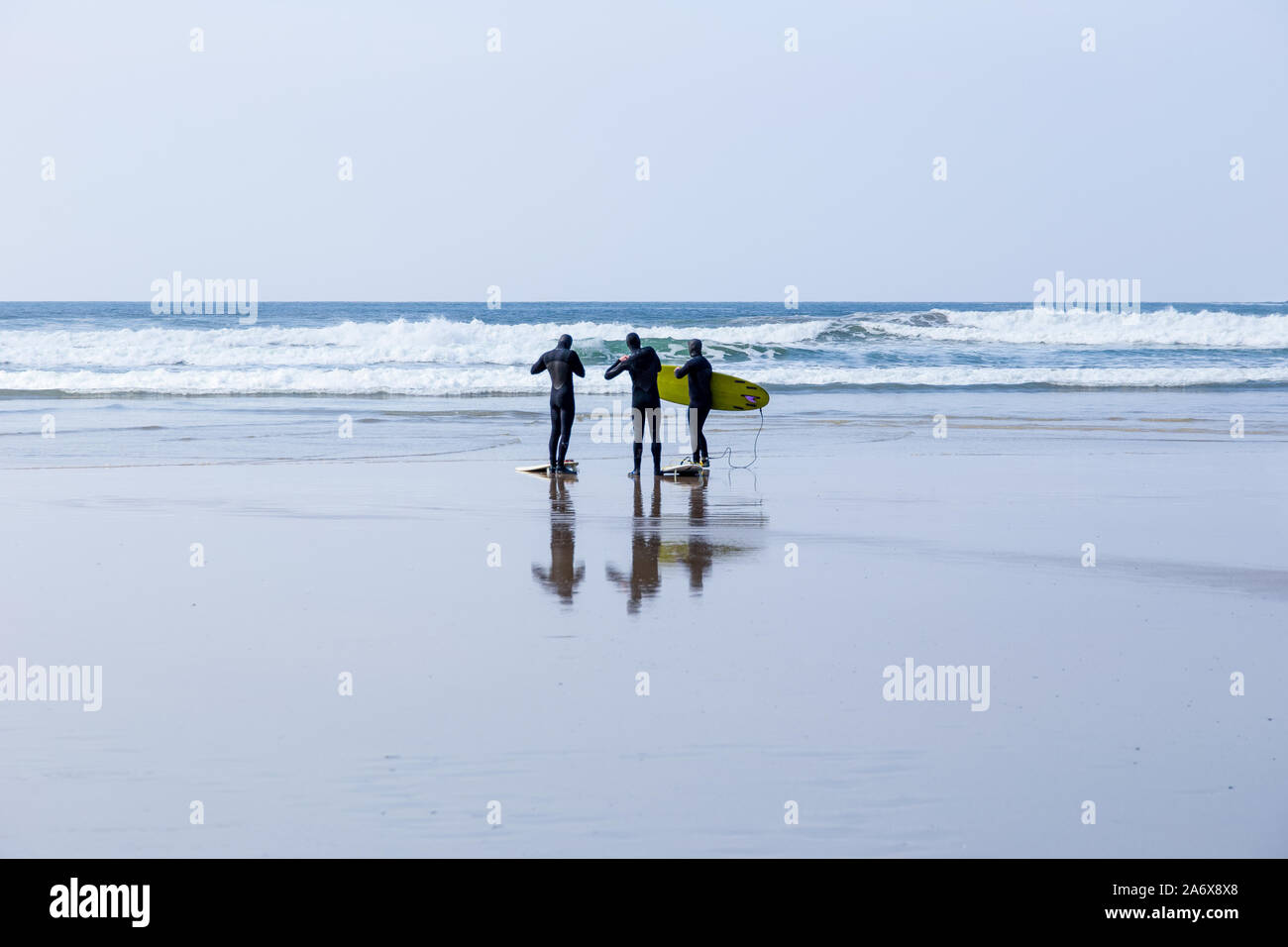 Surfers, with surfboards, on a wet beach in Polzeath, Cornwall, UK Stock Photo