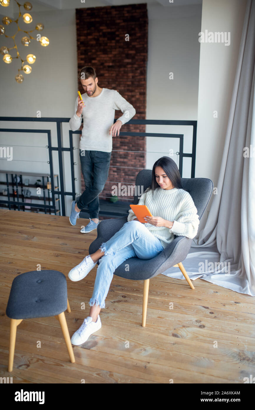 Wife wearing jeans sitting in armchair and using tablet Stock Photo Alamy