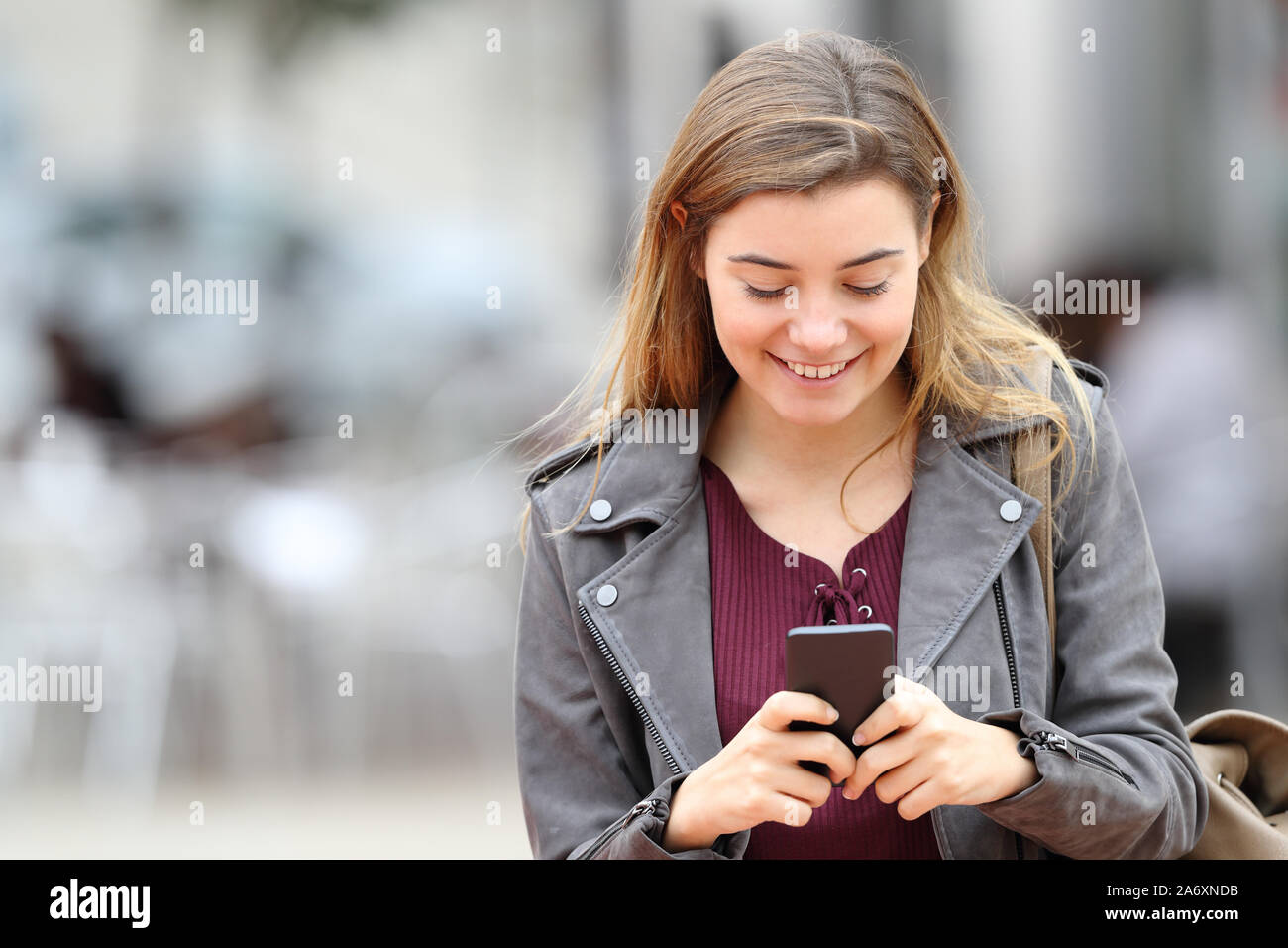 Front view portrait of a happy girl texting on mobile phone in the street with copy space at side Stock Photo