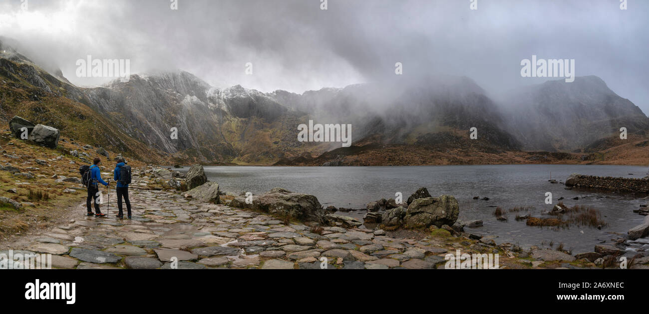 Stunning dramatic Winter landscape image of Llyn Idwal and snowcapped Glyders Mountain Range in Snowdonia with hikers plotting their route Stock Photo