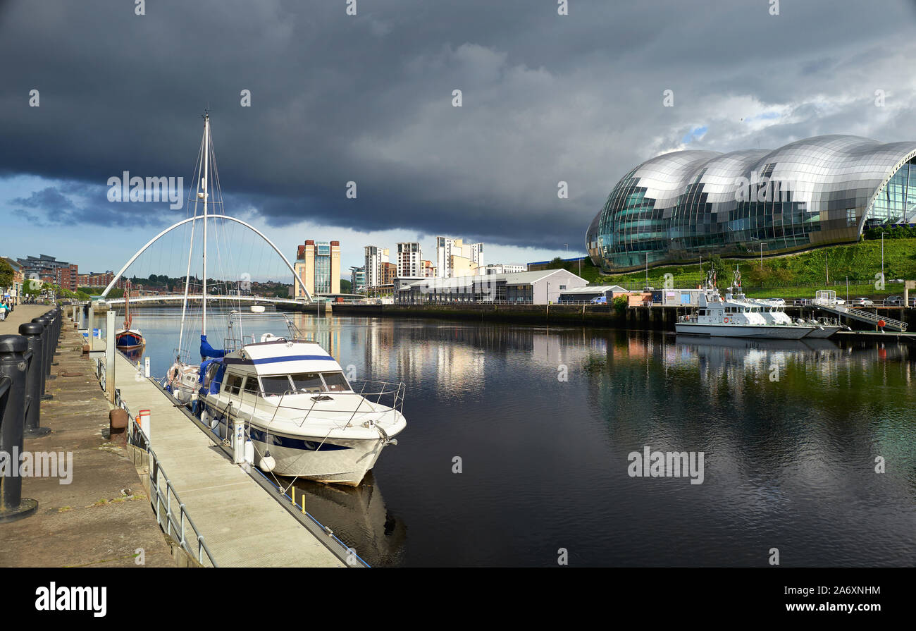 A yacht moored at Newcastle's Quayside with the Baltic Art Museum, Gateshead Sage and Millennium Bridge in the distance. Stock Photo