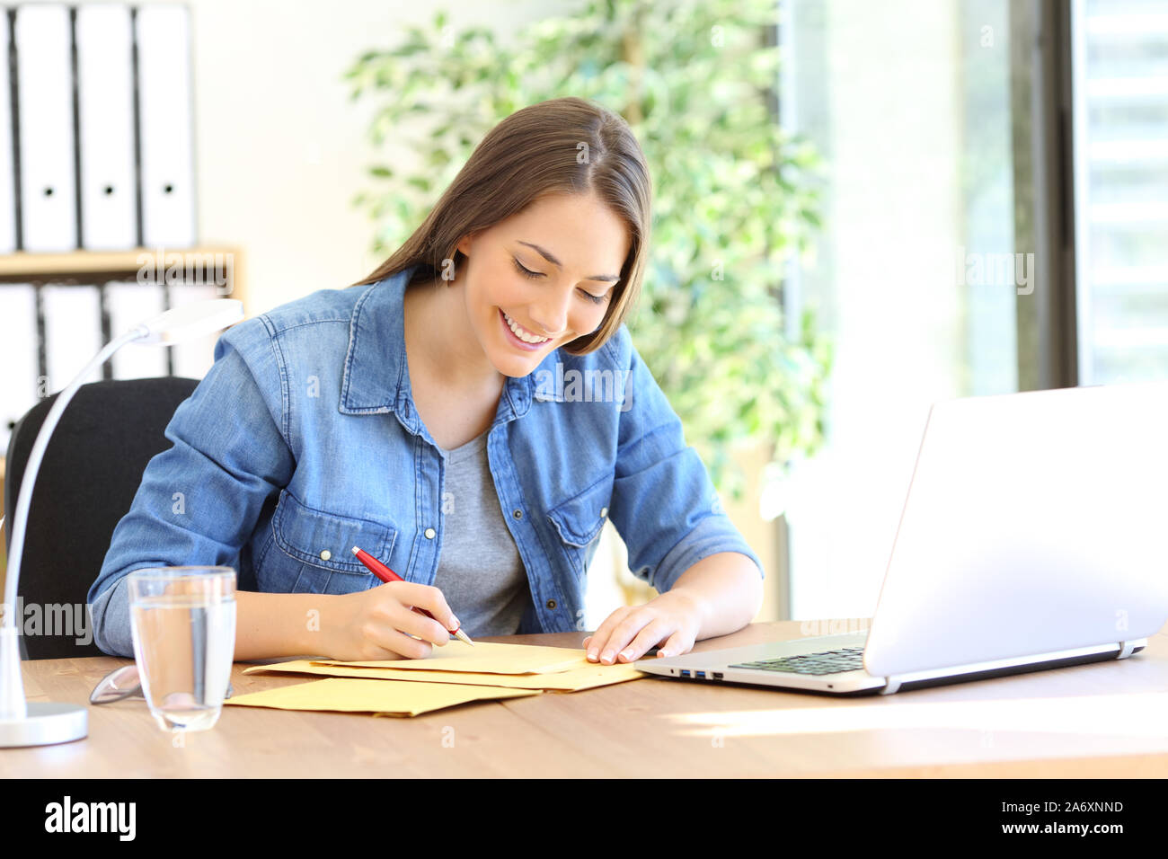 Happy casual entrepreneur writing address on an envelope at office Stock Photo