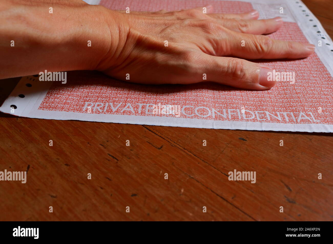 Closeup words private and confidential printed on continuous form paper with left hand pressing on it, selective focus Stock Photo