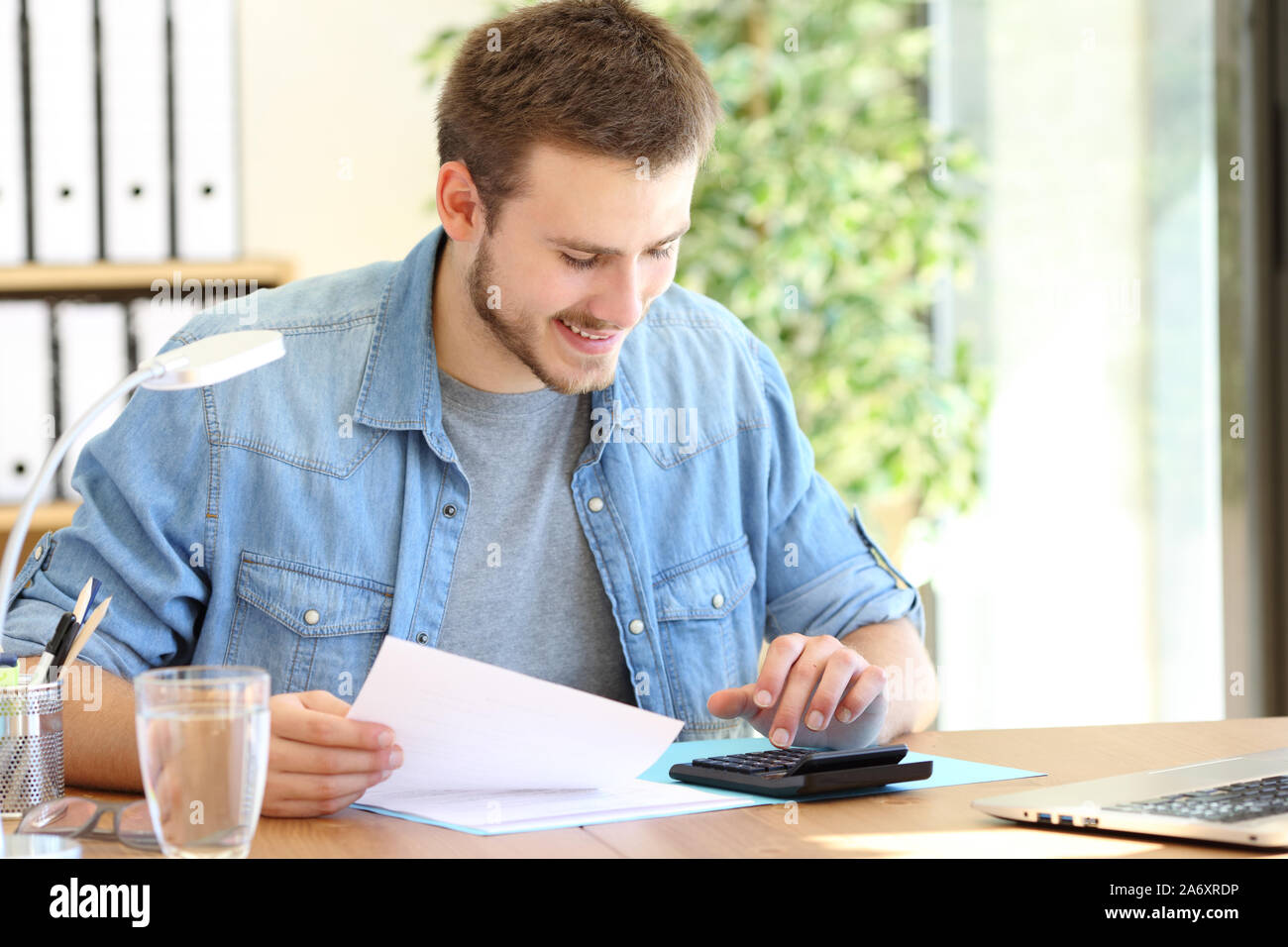 Happy entrepreneur calculating using a calculator sitting on a chair working at office Stock Photo