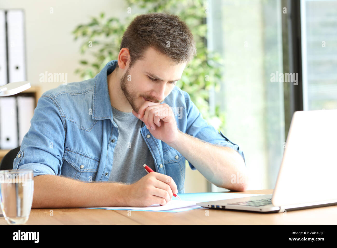 Pensive entrepreneur handwriting using pen sitting on a chair at office ...