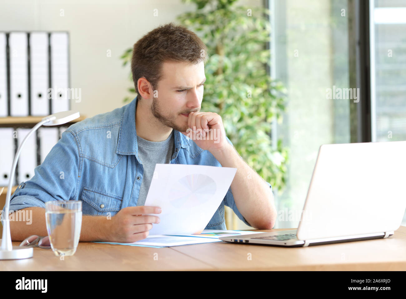 Pensive man holding document reading laptop content working at office Stock Photo