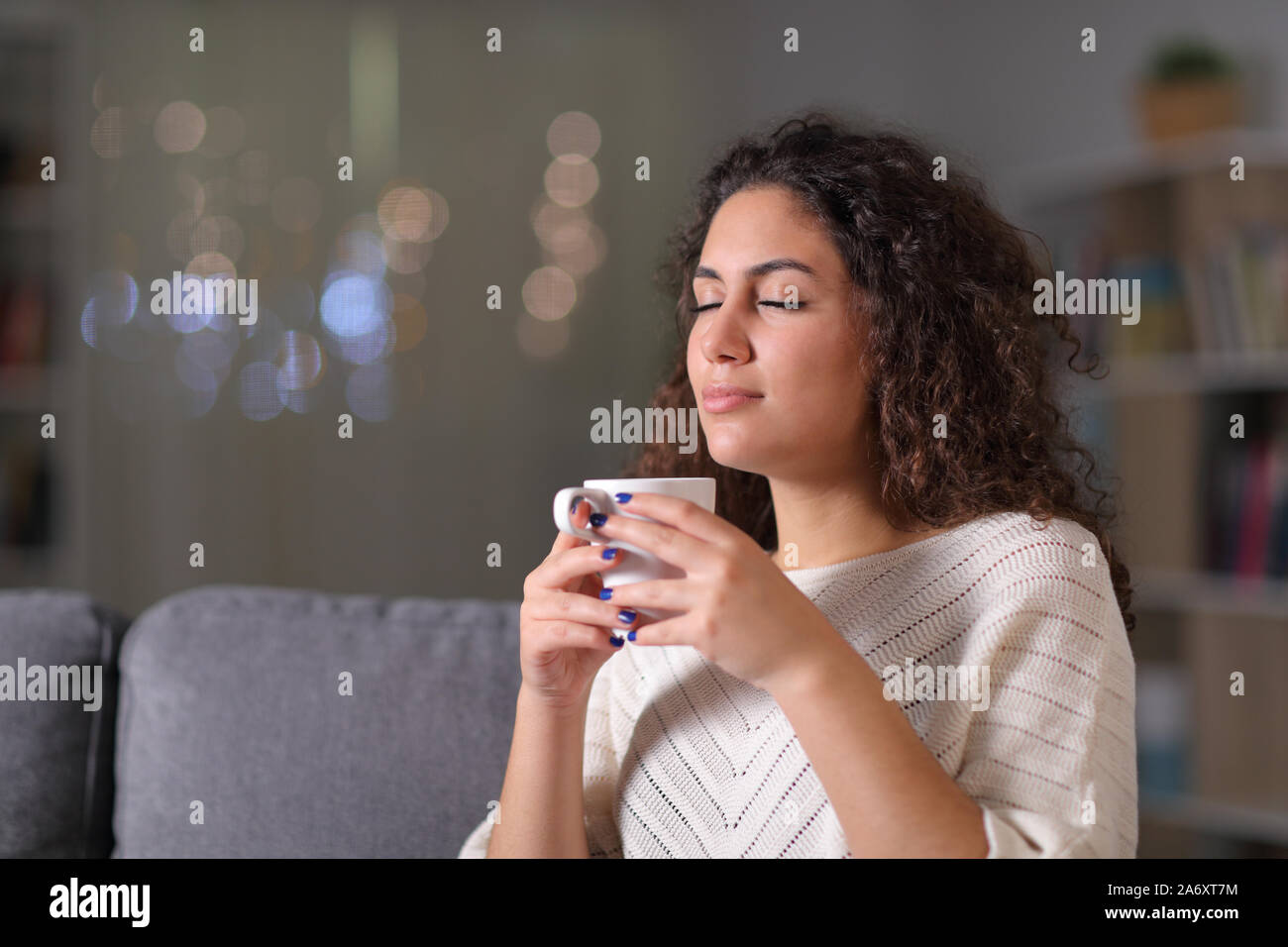 Relaxed woman smelling coffee cup sitting on a couch in the night at home Stock Photo