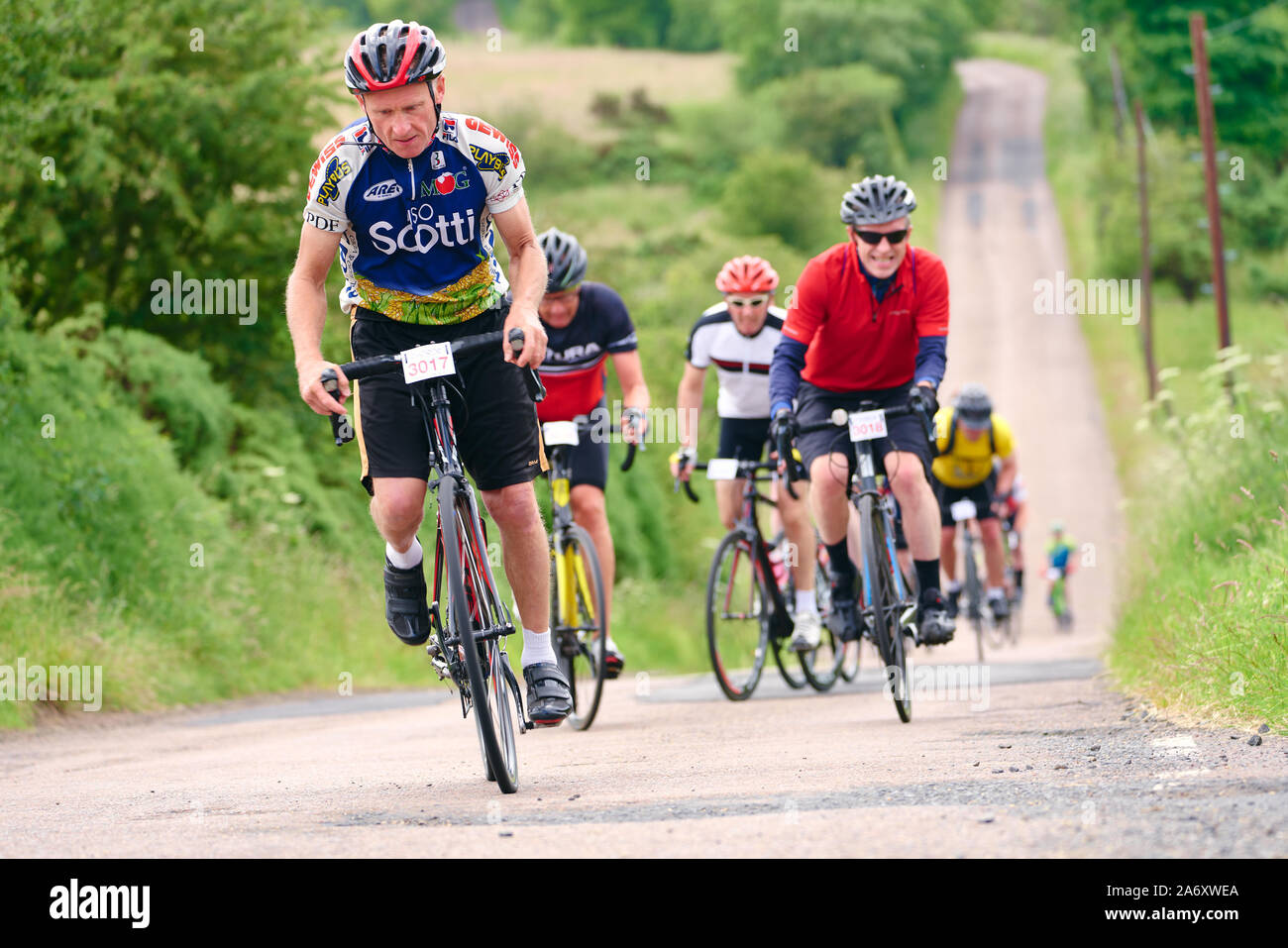 ROTHBURY, NEWCASTLE UPON TYNE, ENGLAND, UK - JULY 06, 2019: Cyclists working hard peddling up a steep hill at the cyclone race event from Newcastle to Stock Photo