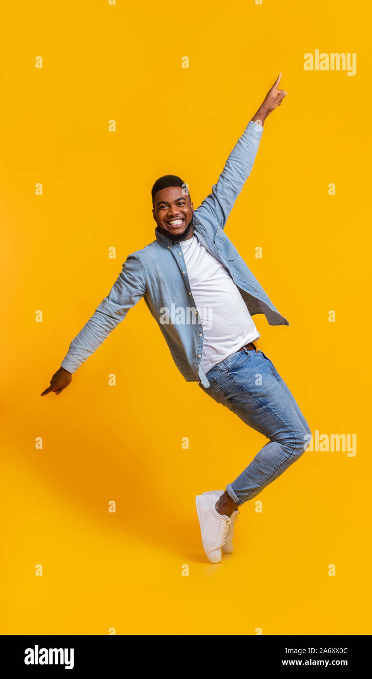 Cheerful African Man Standing On Tiptoes, Fooling Over Yellow Background Stock Photo