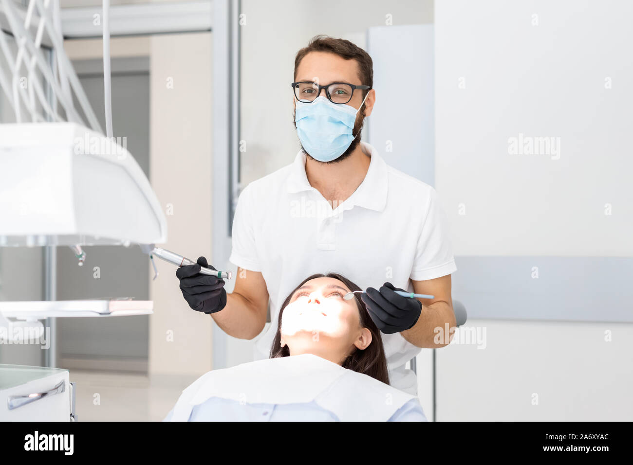 Dentist doctor with glasses drilling teeth to female patient Stock