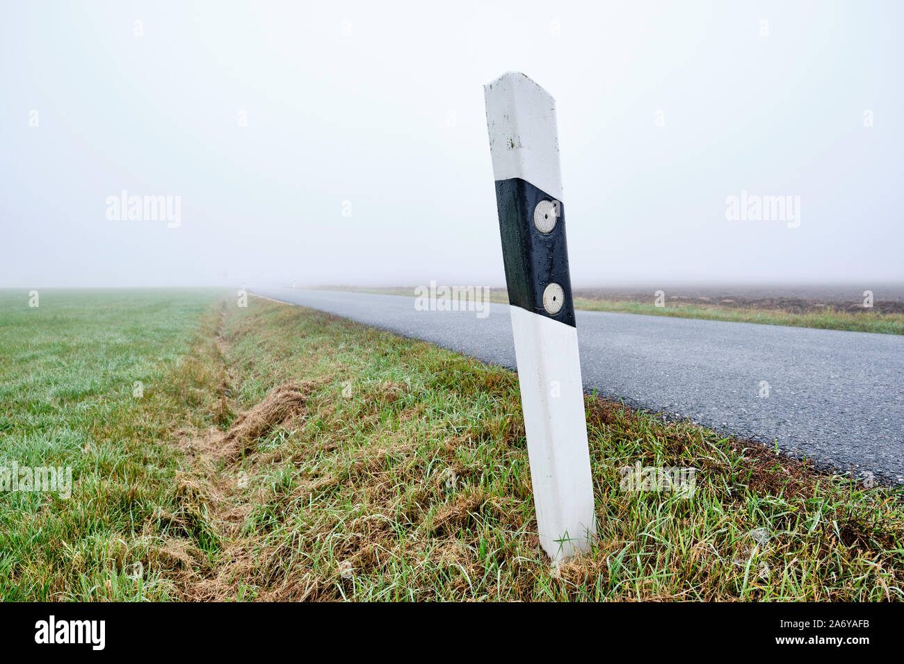 Lonesome reflector post at countryside road to nowhere -  narow street with diminishing perspektive leading into the fog. Seen in Germany near Oedenbe Stock Photo