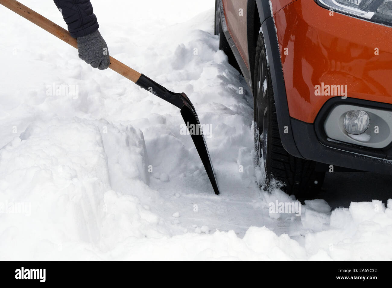 Man with shovel clears snow around car in parking lot in winter after snowfall. Shovel in hand. Winter problems of car drivers. Stock Photo