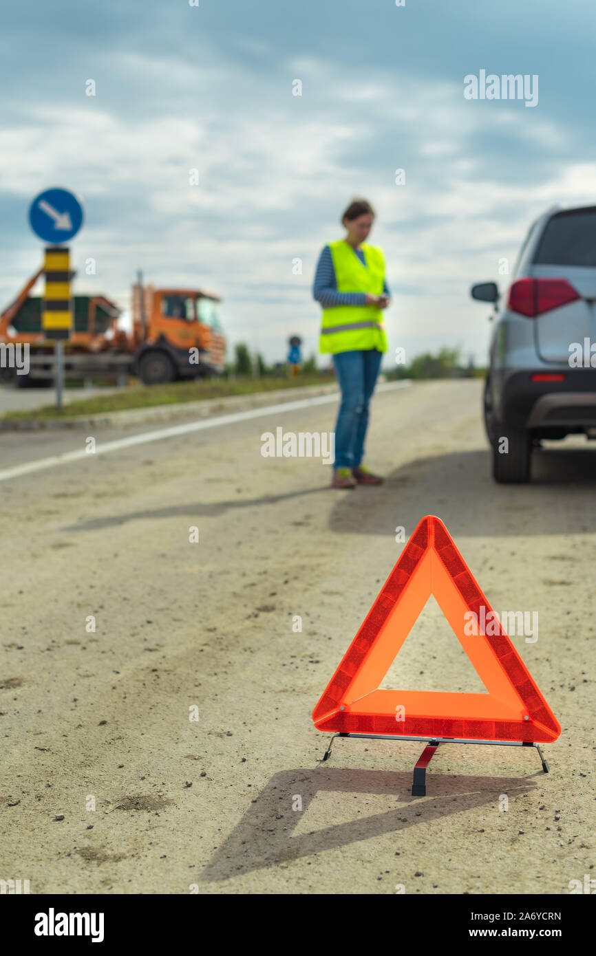 Vehicle breakdown and warning triangle on the road, woman using phone to ask for help and roadside assistance Stock Photo