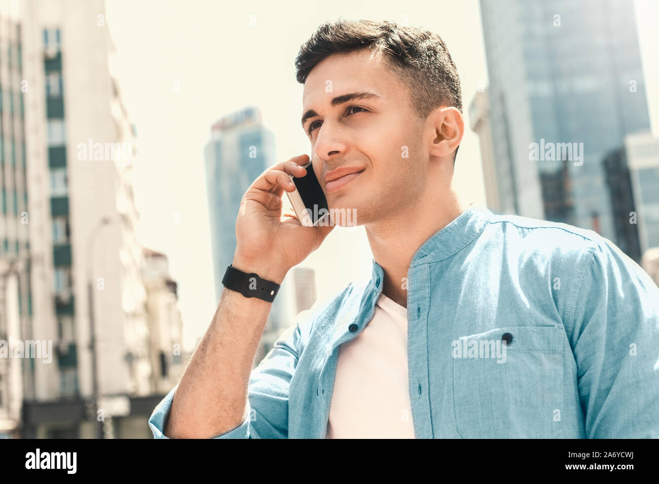 Outdoors Leisure. Stylish guy standing on the street talking on smartphone smiling joyful close-up side view Stock Photo