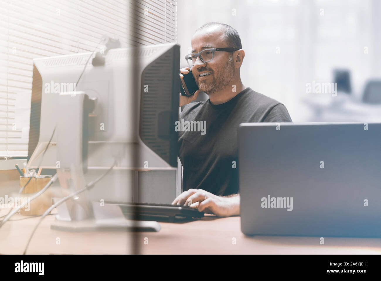 Smiling busy entrepreneur businessman working in the office talking using a mobile smartphone. Workplace and empty copy space for Editor's text. Stock Photo