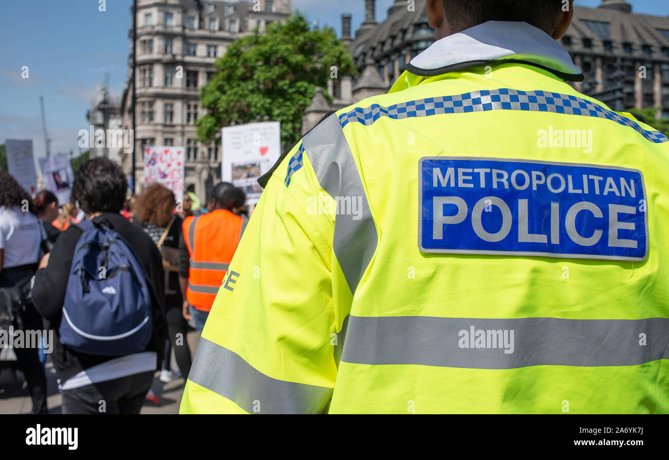 Police officer watches from a distance, while a 'Operation Shutdown' protest demonstration takes place at the gates to the House of Parliament, London Stock Photo