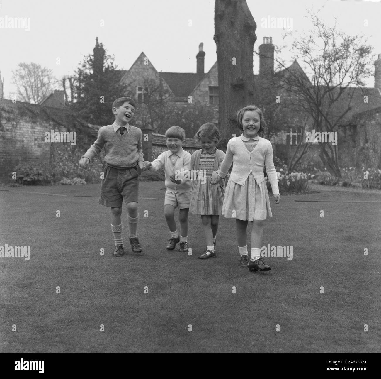 1950s, historical, four well-dressed happy young children holding hands  outside on the lawn of a walled garden of a manor house, England, UK, having attended a Sunday service at the village church. Stock Photo