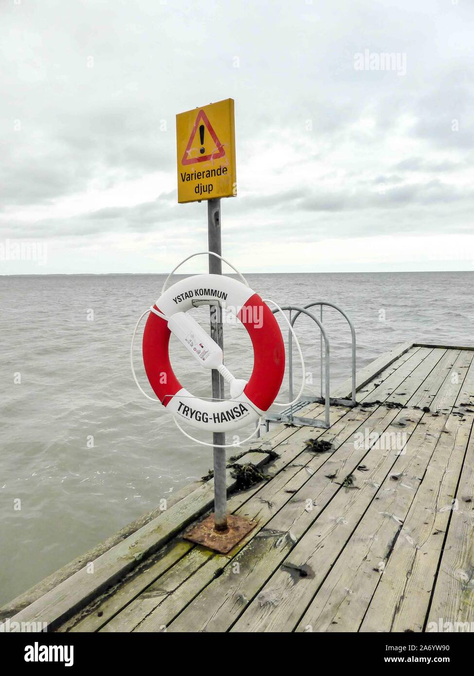Seaside dock in Ystad, Sweden with red and white lifesaver ring mounted on a pole. Stock Photo