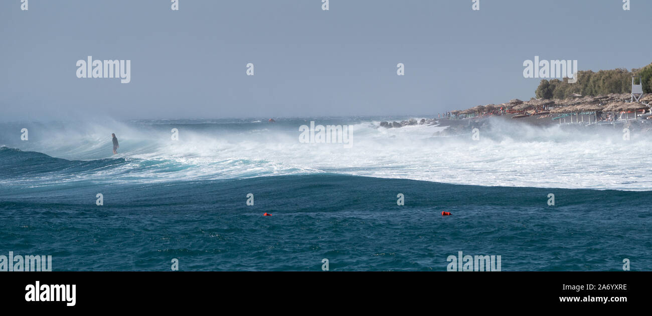 a person standing against facing rough waves on windy stormy Santorini Stock Photo