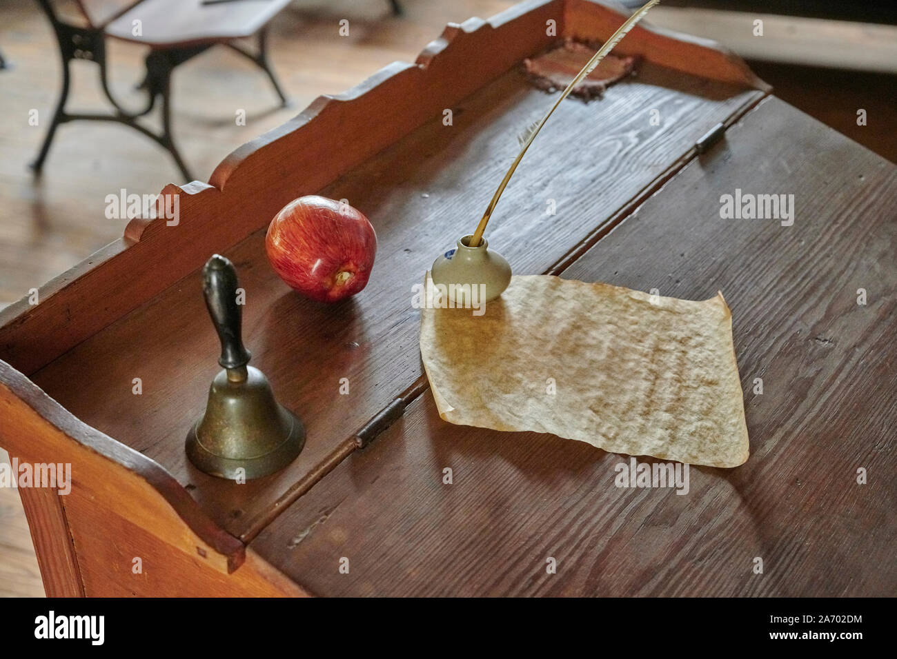 Vintage school teacher podium with an apple, a bell and a quill pen and paper in an 18th Century old schoolhouse or school classroom. Stock Photo