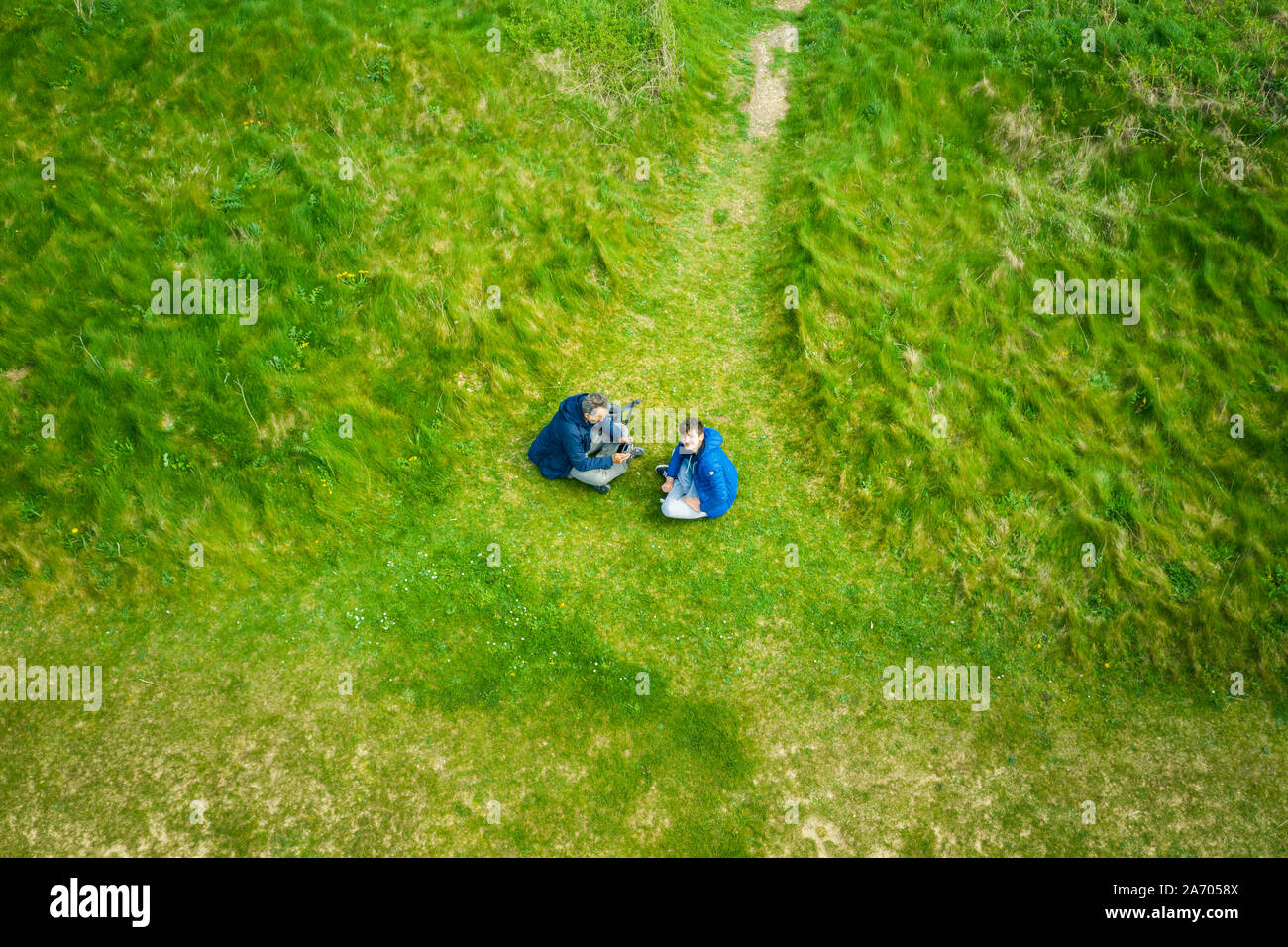 Aerial view of father and son sitting on the grass and flying drone ...