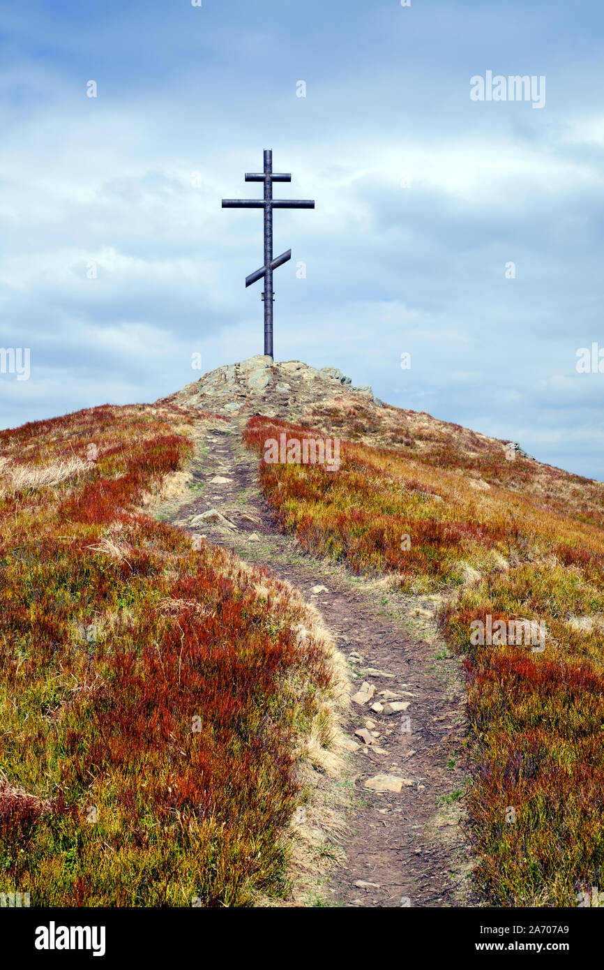 Metal cross on top of the mountain and grassy road leading to him Stock Photo
