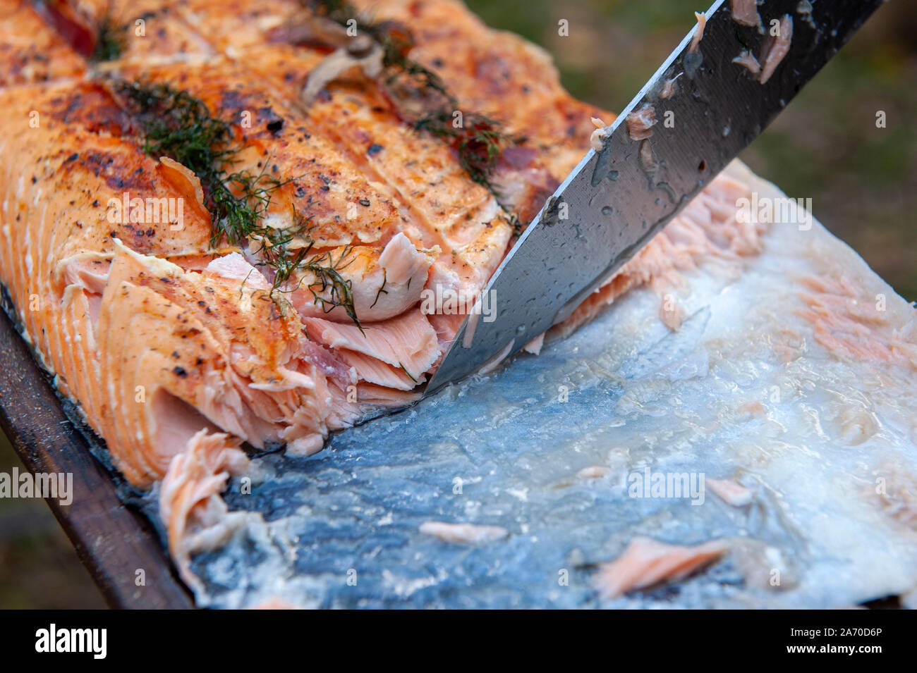 A cook is cutting a piece of salmon with a knife Stock Photo