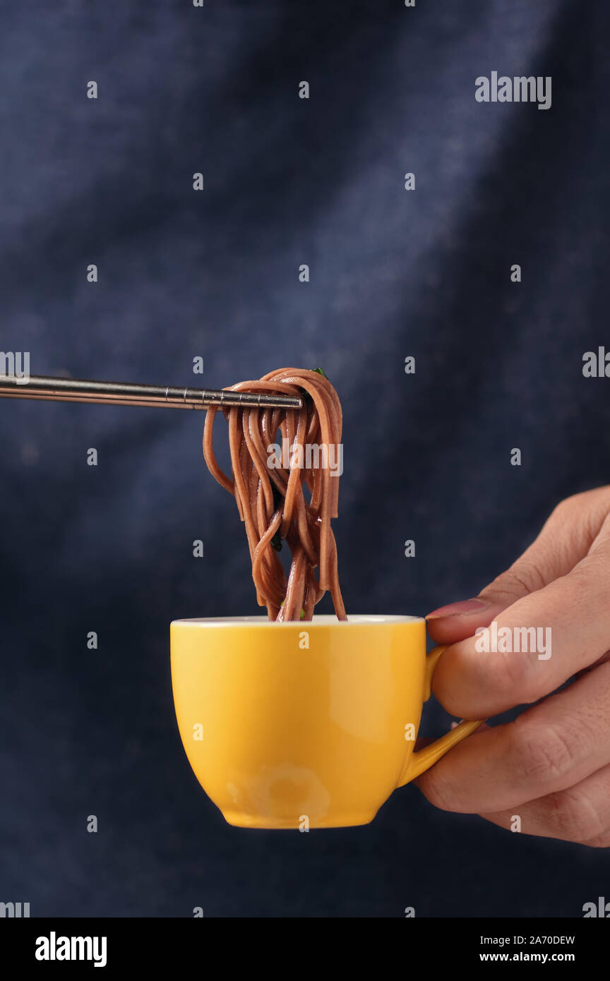 Pick the buckwheat noodle from a cup of dipping sauce by chopsticks