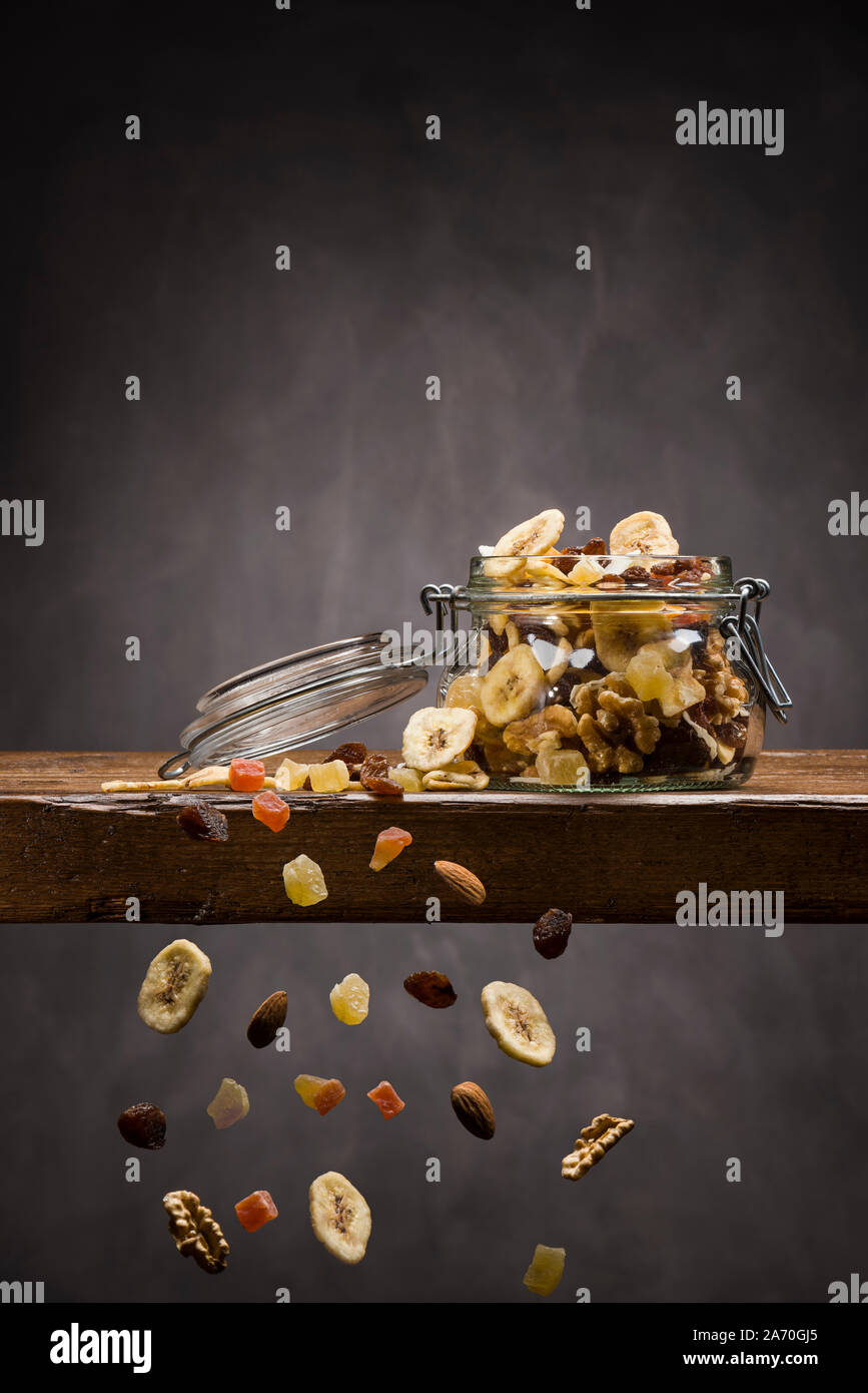 dehydrated fruit in open glass jar on wooden table with fruits falling down Stock Photo