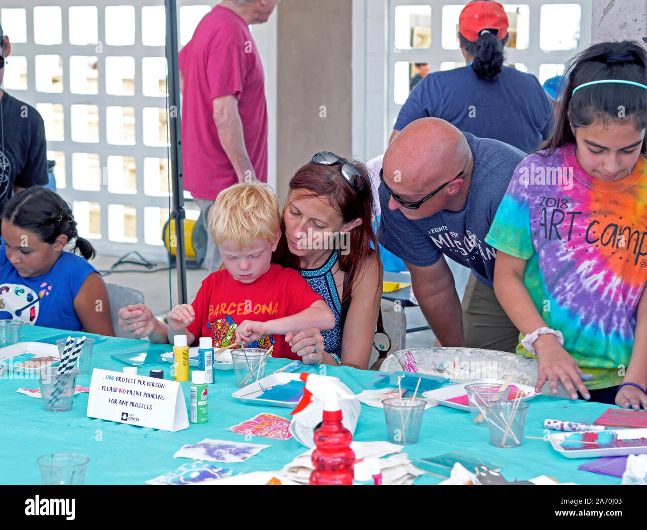 A young Caucasian boy creates art while seated on mothers lap with father watching. Arts Alive Festival 2019 in Corpus Christi, Texas USA. Stock Photo