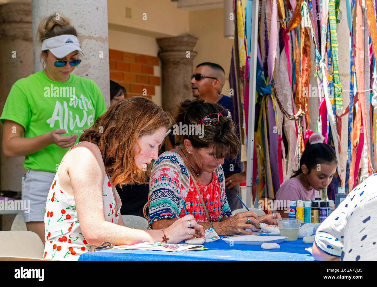 A young redhead Caucasian woman at a rock painting table. Arts Alive Festival 2019 in Corpus Christi, Texas USA. Stock Photo