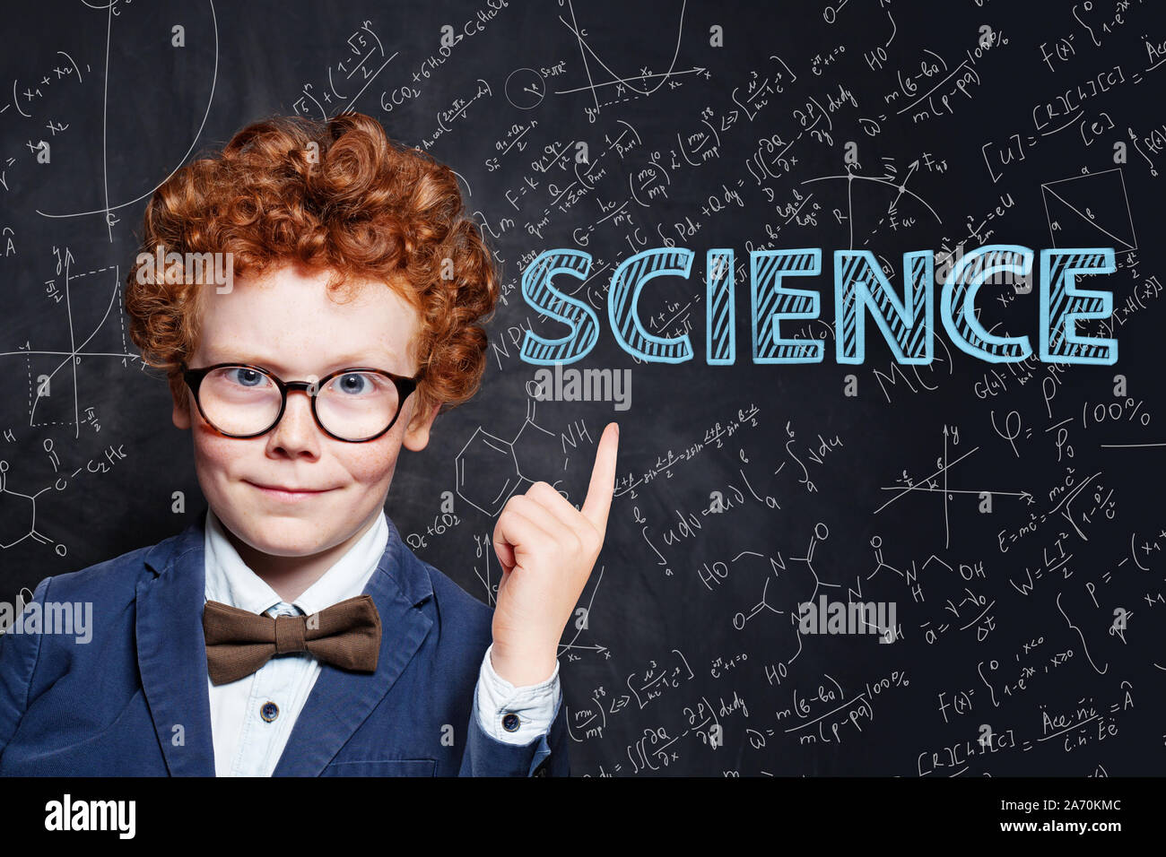 Confident kid little boy with ginger hair pointing at science inscription on chalkkboard background Stock Photo