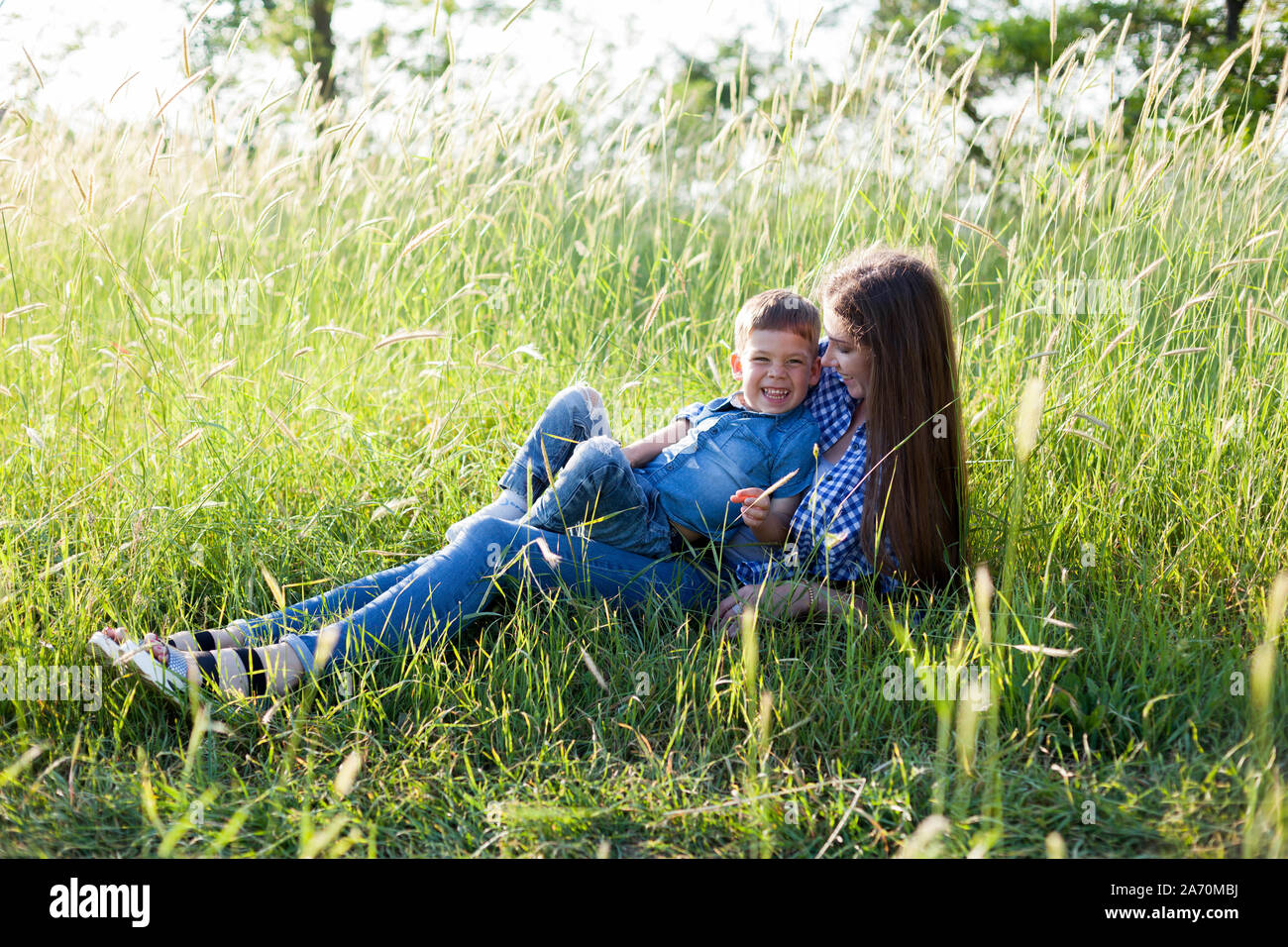 Mom and little son lie on the grass in the woods Stock Photo