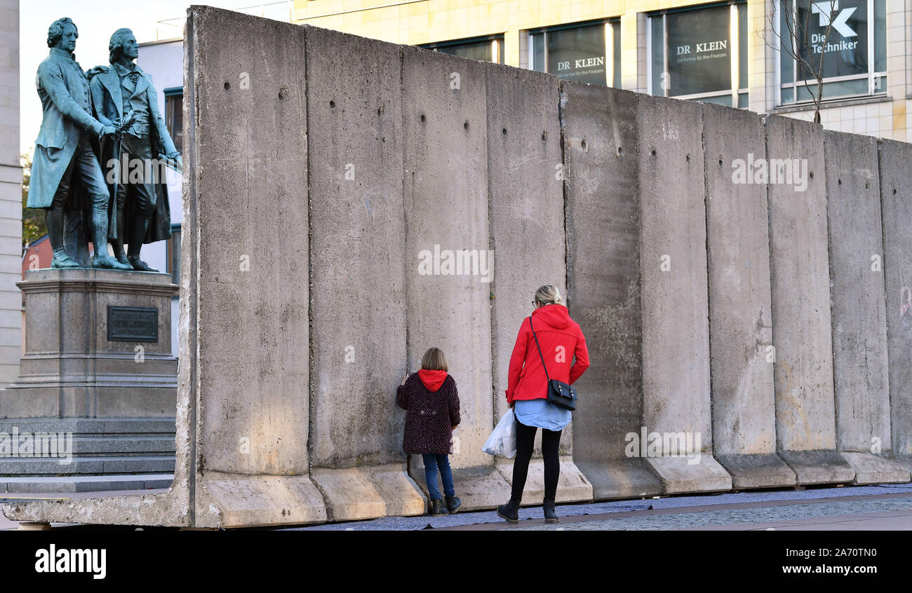 Weimar, Germany. 29th Oct, 2019. Passers-by walk along the wall  installation "Horizons" in memory of the fall of the Berlin Wall in 1989 in  front of the Goethe Schiller Monument and the