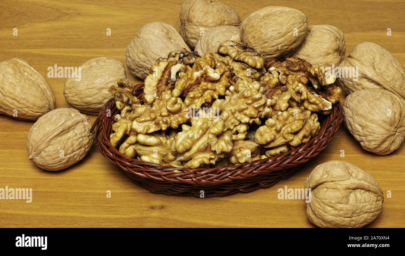 some walnuts around a small basket full of kernels Stock Photo