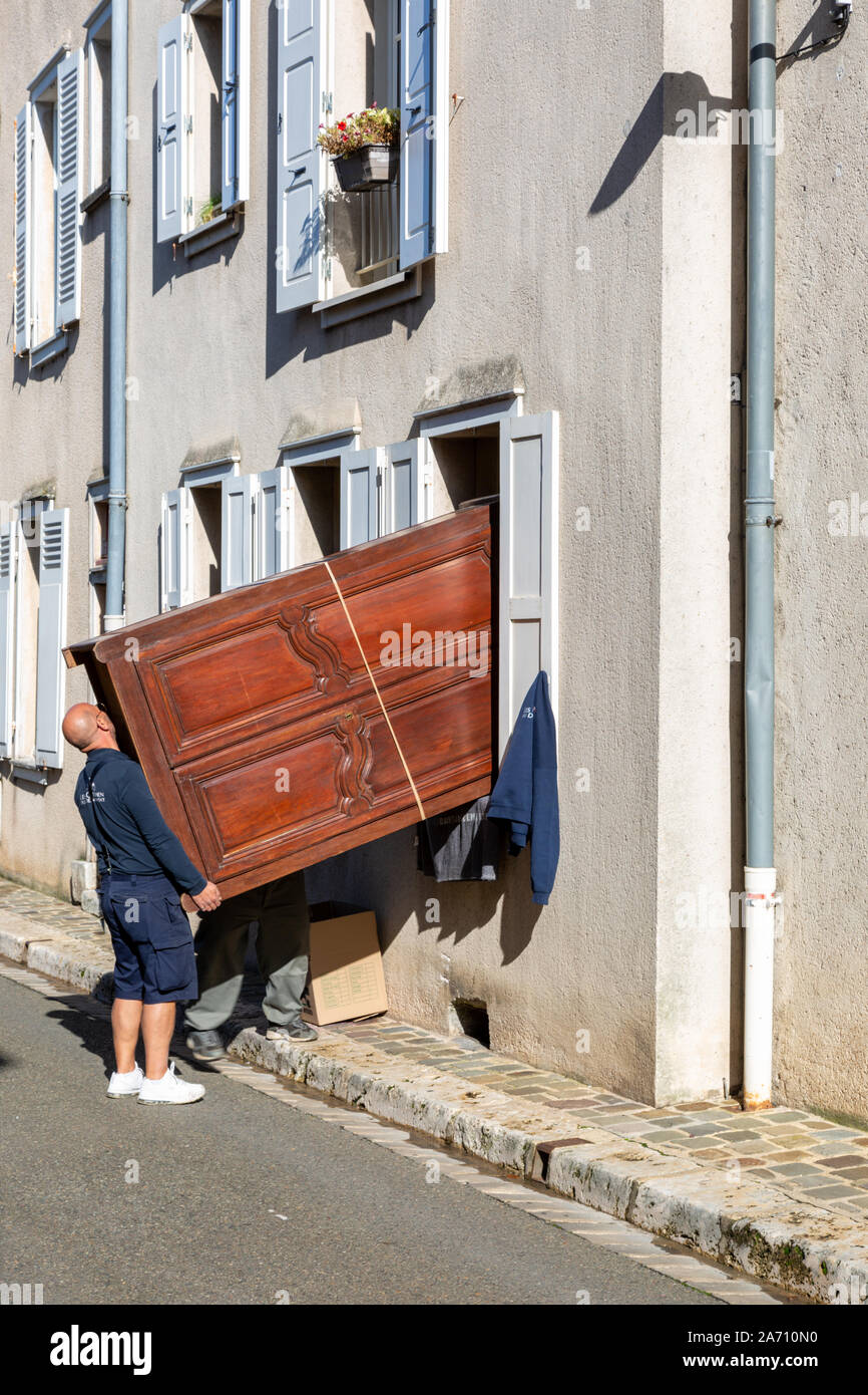 Two men lifting a large wardrobe into a house through a window, France Stock Photo