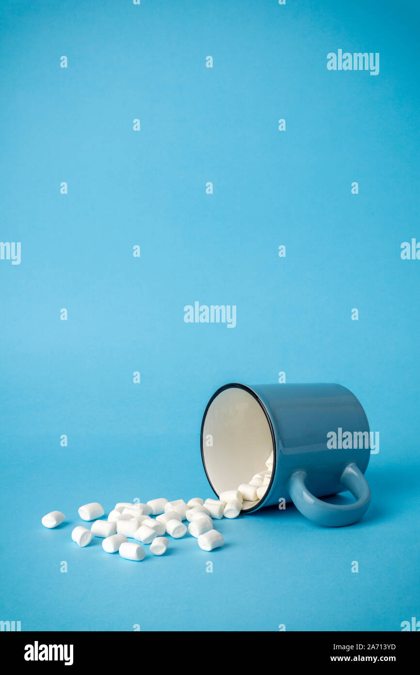 Overturned cup with marshmallows on a blue background. Cocoa drink concept. Stock Photo