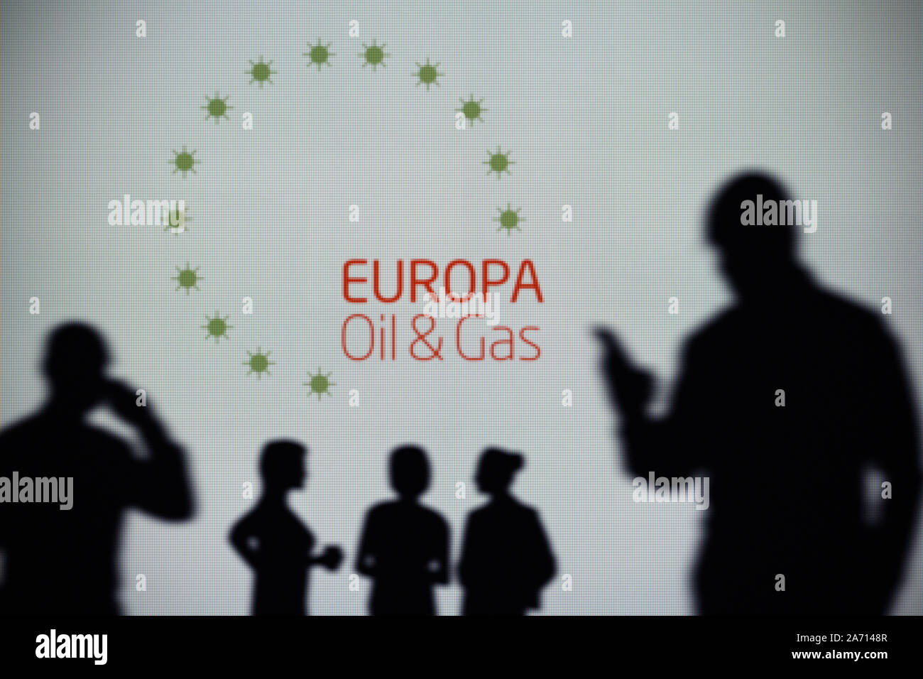 The Europa Oil & Gas logo is seen on an LED screen in the background while a silhouetted person uses a smartphone (Editorial use only) Stock Photo