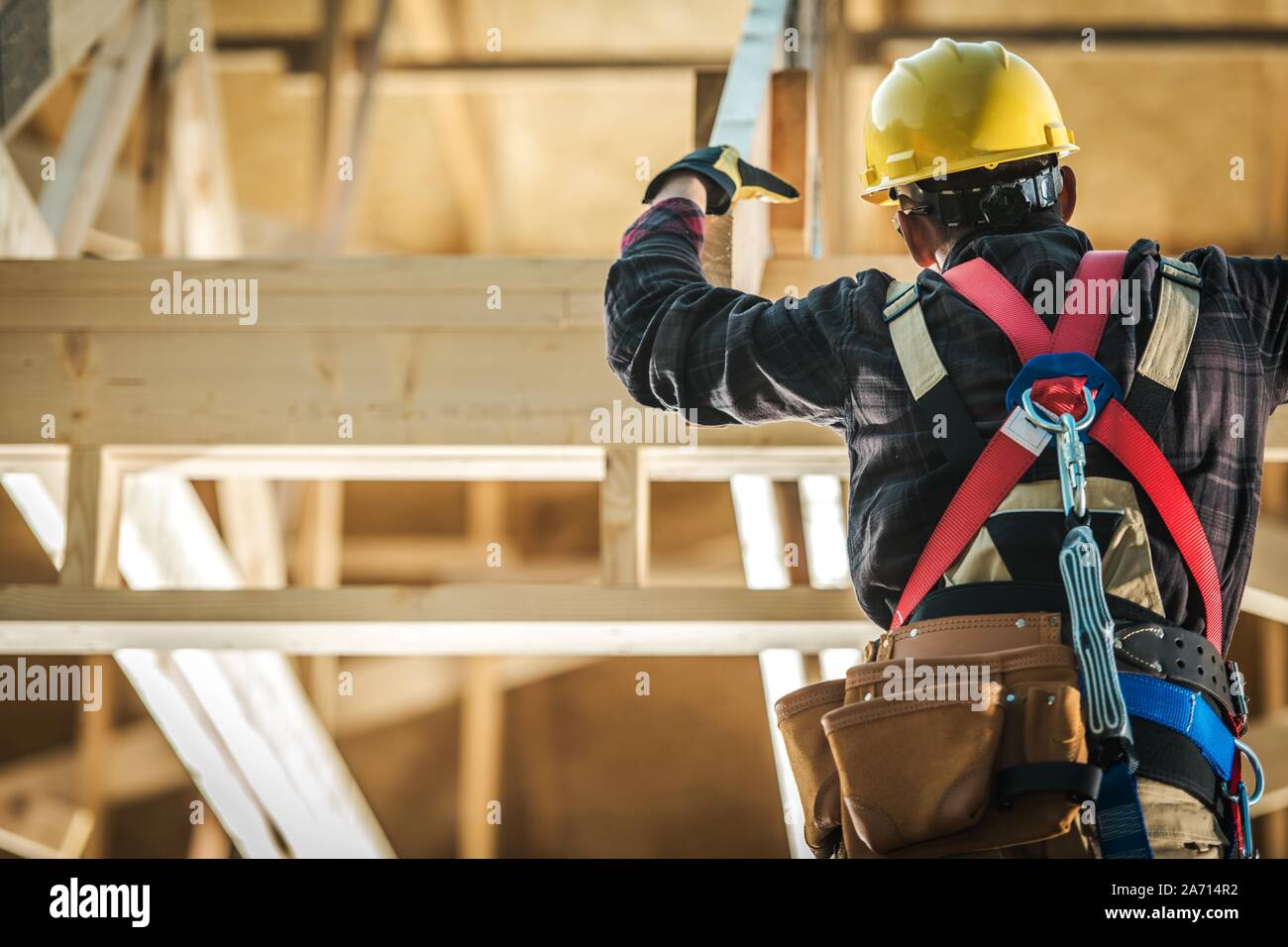 Wood Construction Worker. Caucasian Builder Wearing Safety Harness and the Wooden House Structure. Industrial Theme. Stock Photo