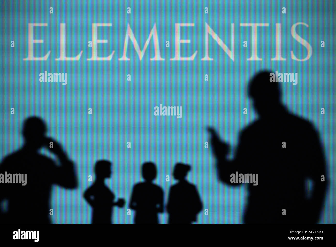 The Elementis logo is seen on an LED screen in the background while a silhouetted person uses a smartphone (Editorial use only) Stock Photo