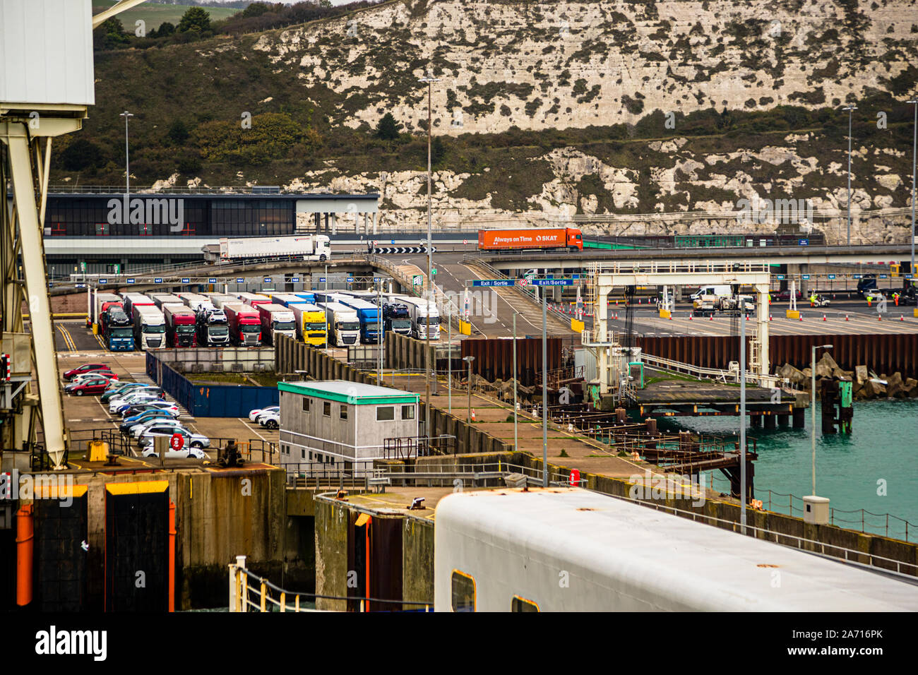 Lorries queue in several lanes for customs clearance at the ferry port of Dover, England. In the cramped harbour area there is little space to evade when traffic comes to a standstill due to the checks. Behind them rise the White Cliffs of Dover, the town's chalk landmark. Stock Photo