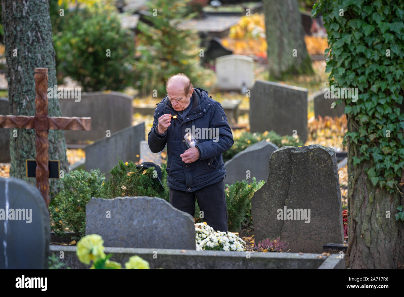 The man visits the graves of relatives and lights a candle in Vilnius Cemetery, Lithuania. The graves are decorated with flowers and candles Stock Photo