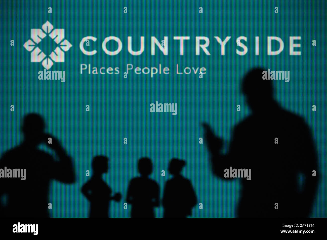 The Countryside Properties logo is seen on an LED screen in the background while a silhouetted person uses a smartphone (Editorial use only) Stock Photo