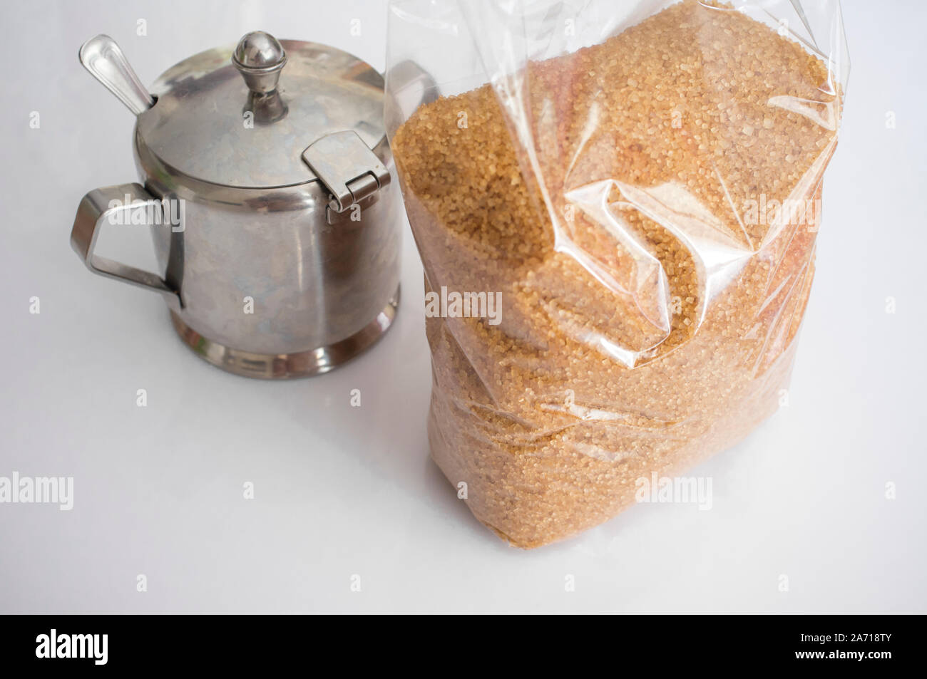 Plastic bag of brown sugar with metal sugar bowl behind. Closeup Stock