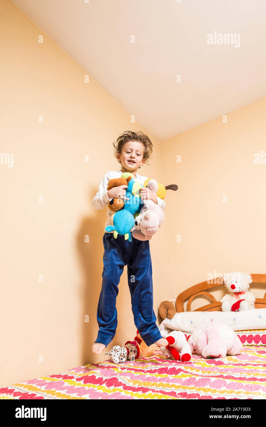 Child with lots of cuddly toys in his arms, jumping on the bed Stock